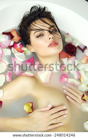 Beautiful young sexy girl with dark hair wet, evening makeup, takes bath with milk tan perfect white skin light tan in romantic atmosphere, beauty cosmetic salon and spa for woman at Valentine\'s Day