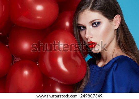 Beautiful young sexy girl with long hair brunette woman with evening make-up cosmetics dressed in a blue silk dress dekzhit in hand many red balloons party Valentine\'s Day heart and love