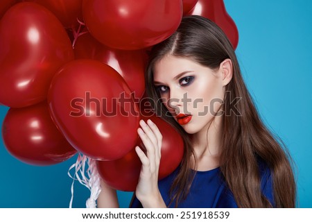 Beautiful young sexy girl with long hair brunette woman with evening make-up cosmetics dressed in a blue silk dress in hand many red balloons party Valentine\'s Day heart and love