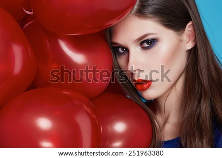 Beautiful young sexy girl with long hair brunette woman with evening make-up cosmetics dressed in a blue silk dress holding in hand many red balloons party Valentine\'s Day heart and love