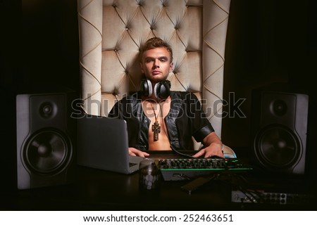 Young stylish trendy guy sitting musician DJ headphones for musical instruments and laptop with speakers