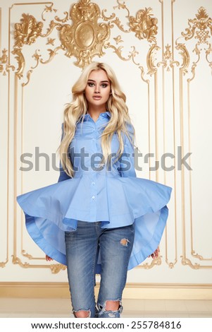 Beautiful sexy young blonde girl with long thick wavy hair thin slender figure perfect body and pretty face make-up wearing a light blue suit delicate and denim high heels