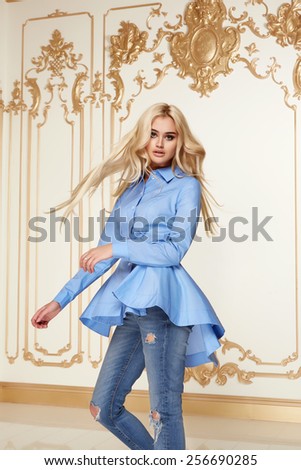 Beautiful sexy young blonde girl with long thick wavy hair thin slender figure perfect body and pretty face make-up wearing a jeans denim and blue blouse high heels