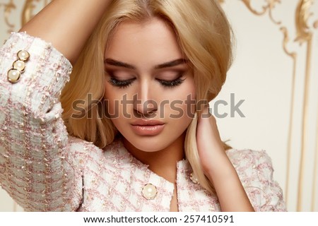 Beautiful sexy young blonde girl with long thick wavy hair thin slender figure perfect body and pretty face make-up wearing a light pink suit
