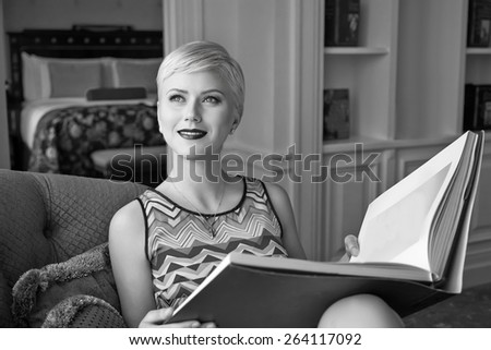 Beautiful young sexy blond woman with short hair blue eyes makeup business woman reading a rest in a room with a book in the luxurious interior