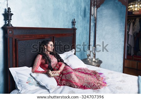 Beautiful young sexy woman with long dark hair brunette and decoration in evening dress of silk lace, room bedroom in Moroccan style velvet pillows luxurious furniture fashion harem concubine bed