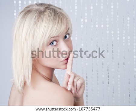 Beautiful young lady with blond hair and with a finger at lips, secret