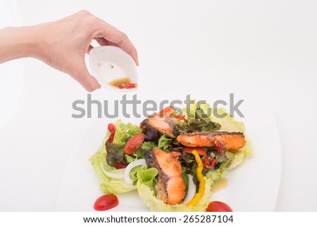 ,green and healthy food salmon salad,Female hand pouring salad dressing onto vegetable salad with smoked salmon with place mat and stone kitchen counter top underneath white dinner plate