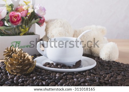 Vintage tone,Teddy bear and flower in vase and cup and saucer on coffee beans on a wooden table