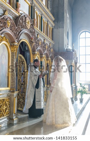 MOSCOW - MARCH 10: bride and groom stand opposite the priest near iconostasis in the rays of light during orthodox wedding ceremony on March 10, 2013 in Moscow