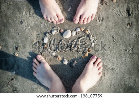 Feet of loving couple and a heart made ??of seashells on the sand on the beach