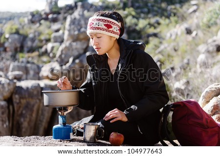 Portrait of an asian chinese backpacker cooking on a camping gas stove while hiking and exploring on a tourist adventure in the wilderness mountains