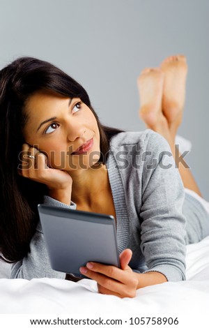 woman reading a modern computer tablet device while lying in bed thinking and wondering to herself