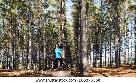 Woman trail running in the woods and jumping over logs while on extreme outdoor fitness training in forest.