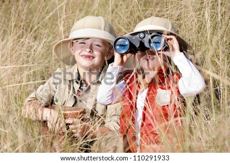 Children brother and sister playing outdoors pretending to be on safari and having fun together with binoculars and hats