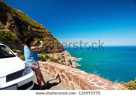 Tourist woman taking a photograph of scenic ocean mountain road chapmans peak in cape town south africa with rental car
