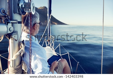 sailing man reading tablet computer on boat with modern technology and carefree retired senior successful lifestyle