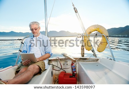 sailing man reading tablet computer on boat with modern technology and carefree retired senior successful lifestyle