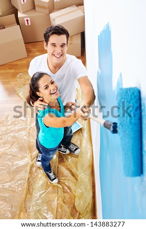 overhead view of couple having fun renovating their new home together with blue paint on a roller