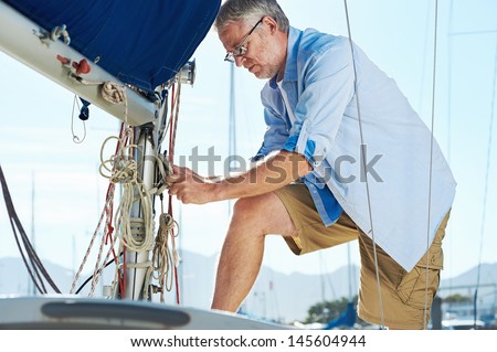 portrait of senior man tying knot and securing a mooring for his hobby yacht sail boat