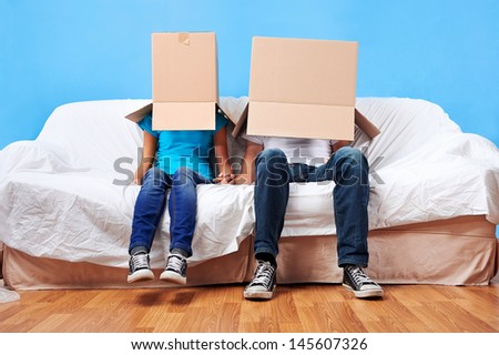 couple sitting on couch with moving boxes on head having fun together