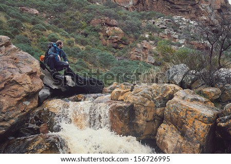 Adventure man crossing river on extreme hike in mountains alone