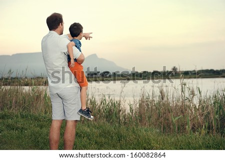 Father pointing out something to son at sunset while holding him in arms