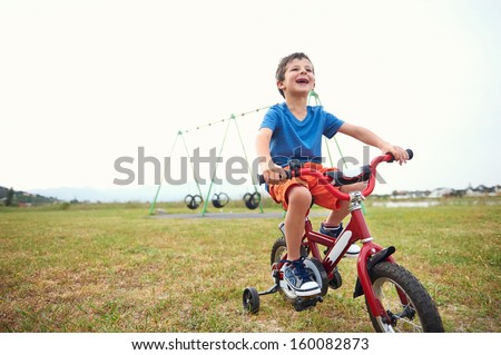 Young boy learning to ride a bike with bicycle training wheels in park