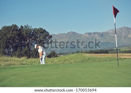 Golfer hitting chip shot from off the green in the rough on scenic golf course