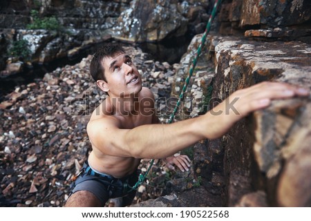 A handsome man with no shirt on rock climbing with copyspace