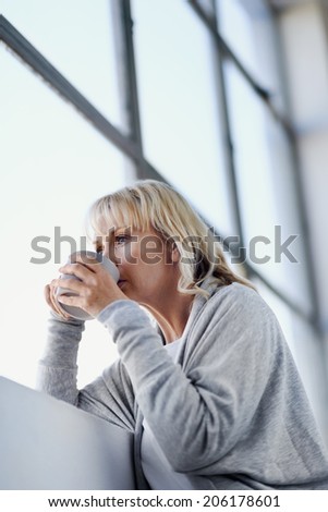 Beautiful blonde woman sipping a cup of tea while looking out the window