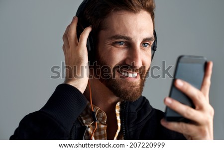 Man with headphones streaming music online with phone enjoying song with beard