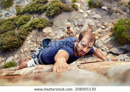 A man reaching for a grip while he rock climbs on a steep cliff