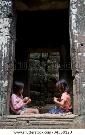 SIEM REAP, CAMBODIA - CIRCA JANUARY 2009: Two young girls make souvenir necklaces at Angkor Wat temple circa January 2009 in Siem Reap, Cambodia. Alledgely, children help to support their families.