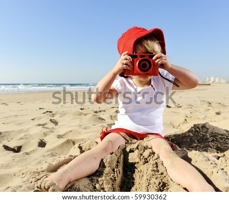 Adorable little girl takes pictures with her red camera on the beach