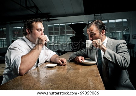 two men share some coffee and look at each other while drinking