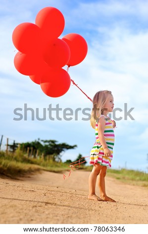 Young caucasian girl walks along a path, holding a bunch of helium filled red balloons