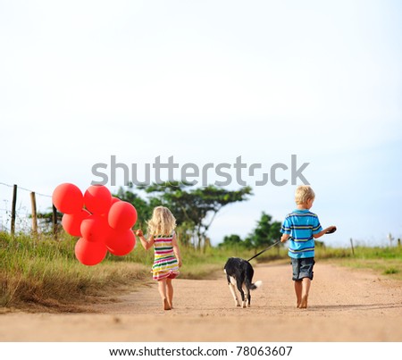 Two blonde children walking along a sandy path with red helium balloons and their puppy towards an adventure