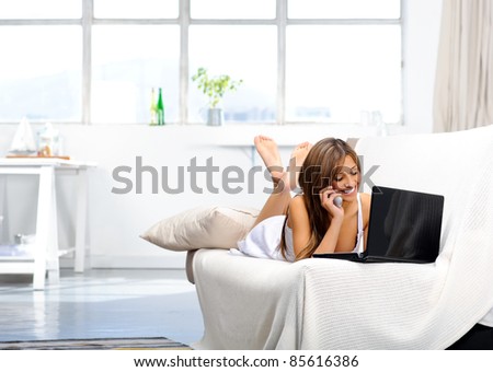 Young woman works from the comforts of her home, reading e-mails from her laptop and chatting to clients on the telephone