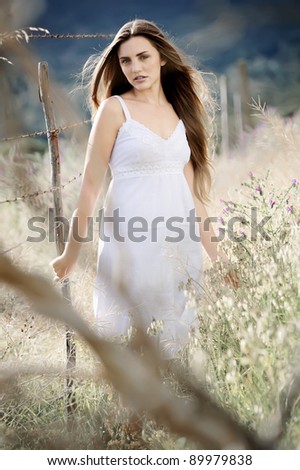 Woman in white dress stands alone in a field, fashion ethereal lonely concept.