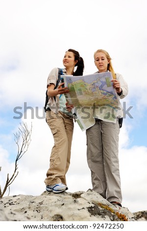 two cheerful women hiking outdoors and consulting their map for the direction in which to travel