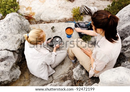 two friendly women cook up some food while camping in the wilderness. outdoor hiking lifestyle concept