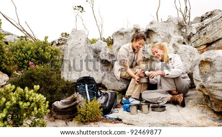 two girls open a can of baked beans while they are camping and hiking in the wilderness