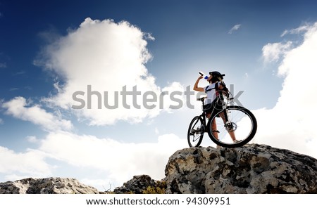 Cyclist drinks water on top of a mountain with bike on a sunny day