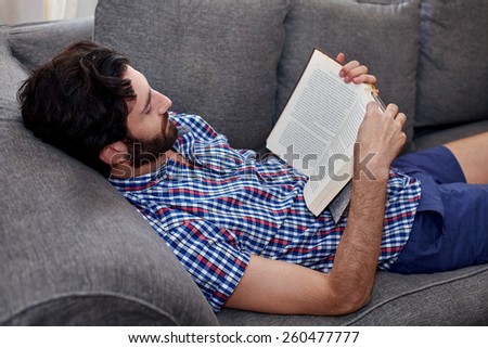 man relaxing on sofa couch reading literature novel story book at home living room lounge