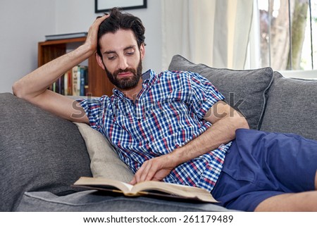 man relaxing on sofa couch reading literature novel story book at home living room lounge