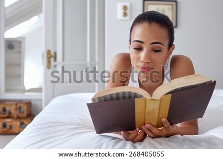 young woman laying relaxing on bed reading literature novel story book at home
