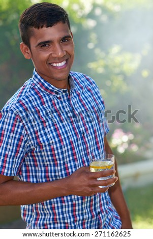 portrait of young indian man standing outdoors in garden with cocktail drink