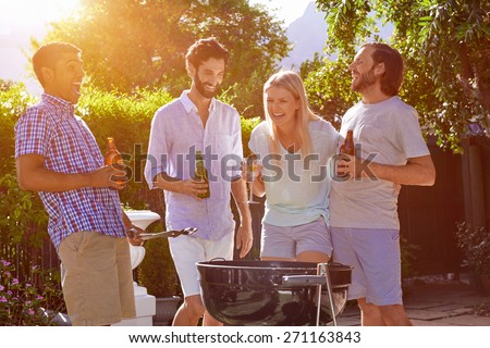 group of friends having outdoor garden barbecue laughing with alcoholic beer drinks