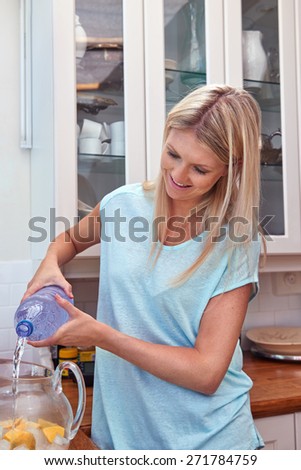 young women pouring water into jug of ice and lemon in the kitchen at home